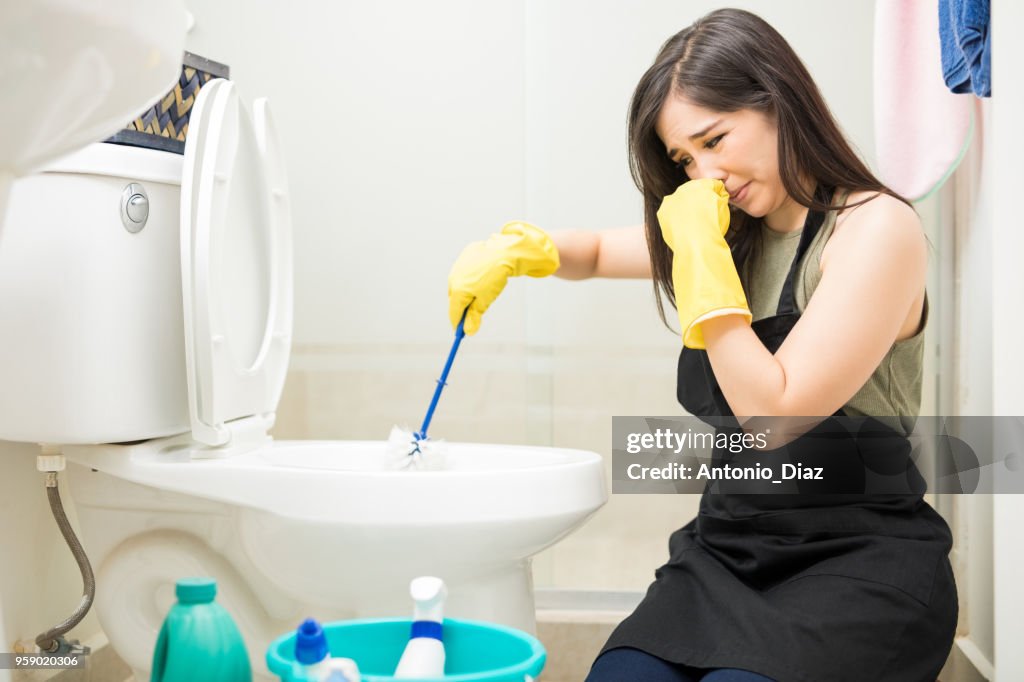 Woman with rubber glove is cleaning toilet bowl using brush