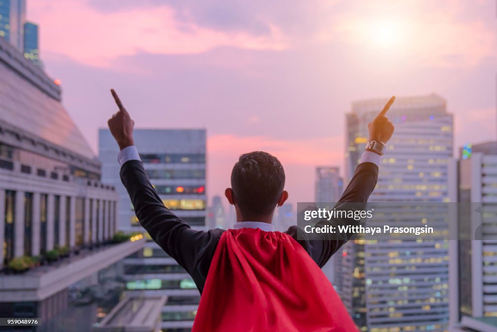 Superhero businessman looking at city skyline at sunset. the concept of success, leadership and victory in business.