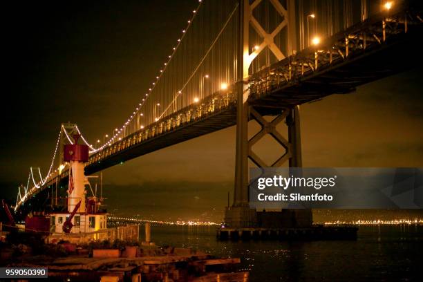 the san francisco bay bridge with fire boat illuminated under night sky - silentfoto stock-fotos und bilder