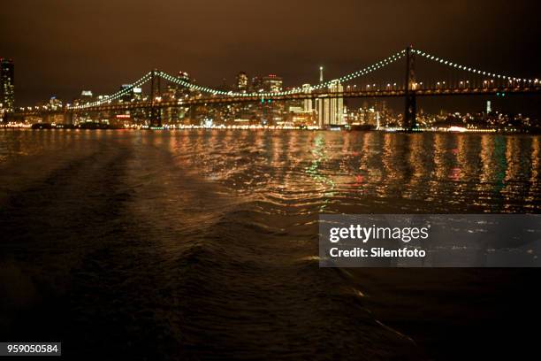 view of san francisco night skyline from aboard ferry crossing sf bay - silentfoto stock-fotos und bilder