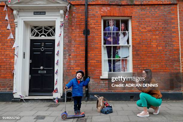 An image of Britain's Prince Harry and his US fiancee Meghan Markle is seen in a window as a woman photographs a child near Windsor Castle in...