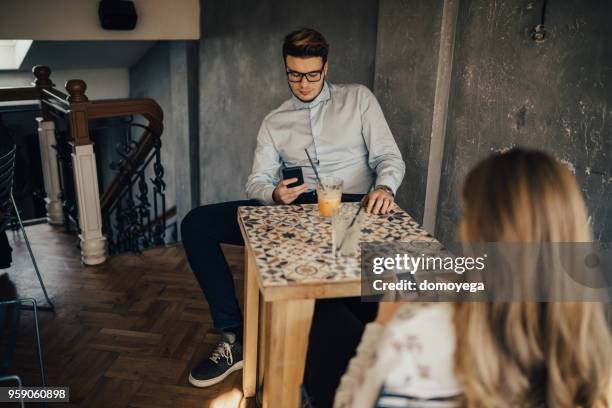 twee mensen met behulp van telefoons tijdens een datum in de koffiebar - bar girl stockfoto's en -beelden