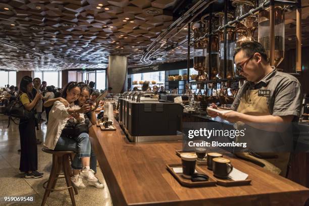 Customers pose for a selfie photograph as coffee beverages are served on a counter inside the Starbucks Corp. Reserve Roastery store in Shanghai,...