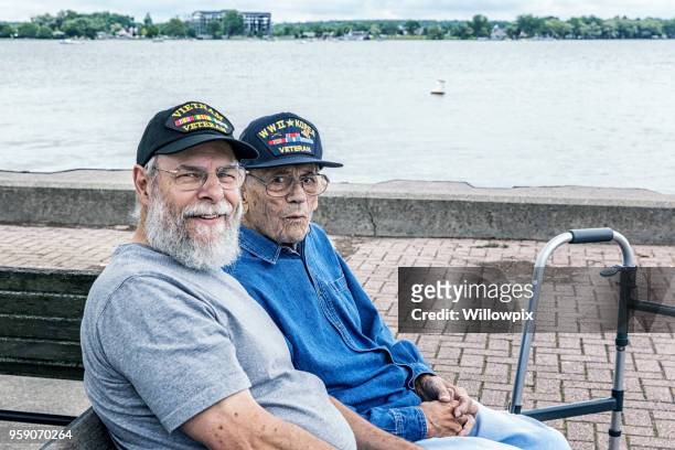 two generations of senior adult usa military veterans sitting at the lake - vietnam war photos stock pictures, royalty-free photos & images