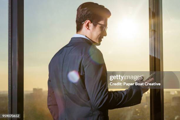 young asian man checks his phone against an overlooking view of the sunset in the city - タギグ ストックフォトと画像