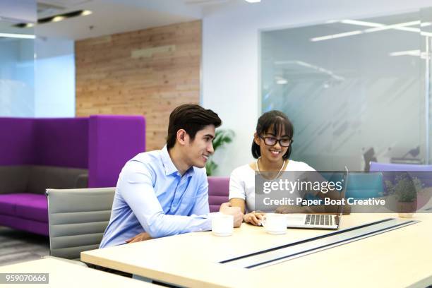 young asian man and woman having a business meeting looking at the laptop over coffee at the office - タギグ ストックフォトと画像