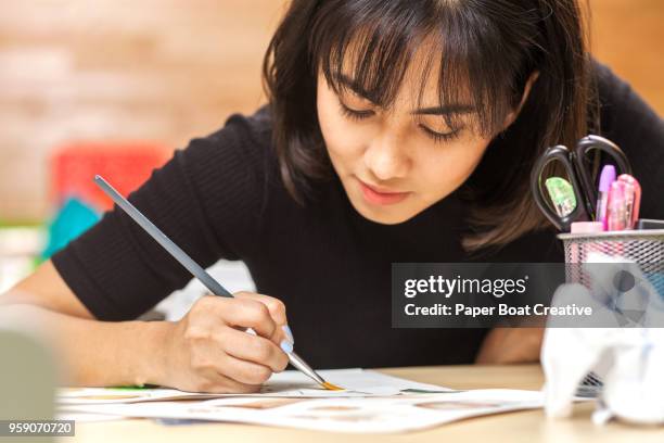 a young asian painter paints inside the office pencils, highlighters and scissors on the table - タギグ ストックフォトと画像