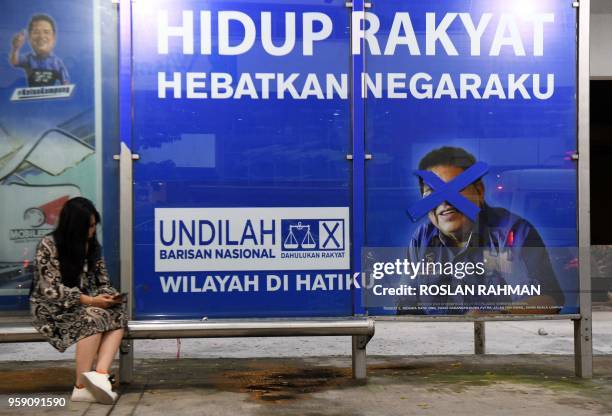 Woman sits at a bus stop with a vandalised campaign poster for Barisan Nasional candidate for Putrajaya, Tengku Adnan Tengku Mansor in Kuala Lumpur...