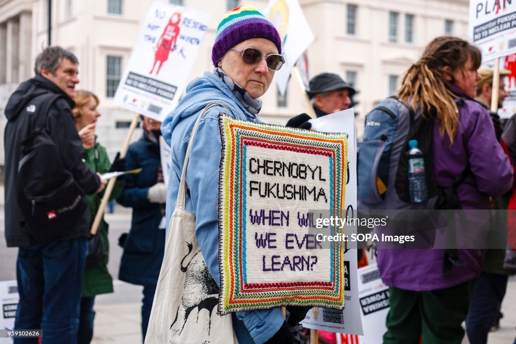 An elderly woman holds a knitted placard referencing the...