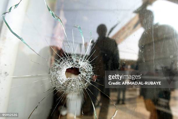 Iraqis are reflected in the bullet damaged window of a near by butchers following an attempted robbery last night in the Iraqi capital Baghdad on...