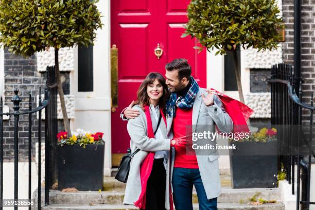 romance couple embracing in front of red door - front door winter stock pictures, royalty-free photos & images
