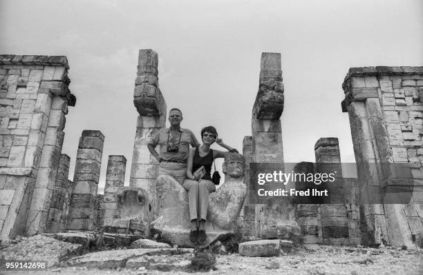 Tourists getting their photograph taken sitting on the Chac Mool statue in the Temple of Warriors, Chichen Itza Maya ruins, Yucatan, Mexico.