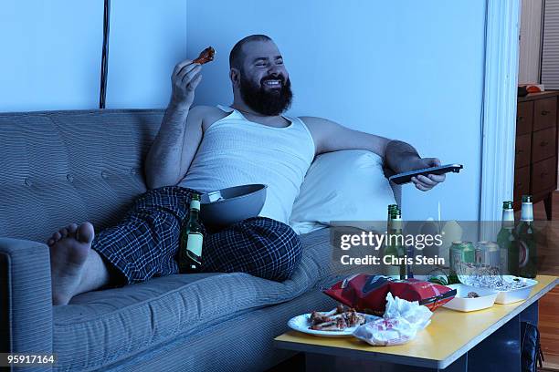 couch potato man with  tv remote - arbeitslosigkeit stock-fotos und bilder