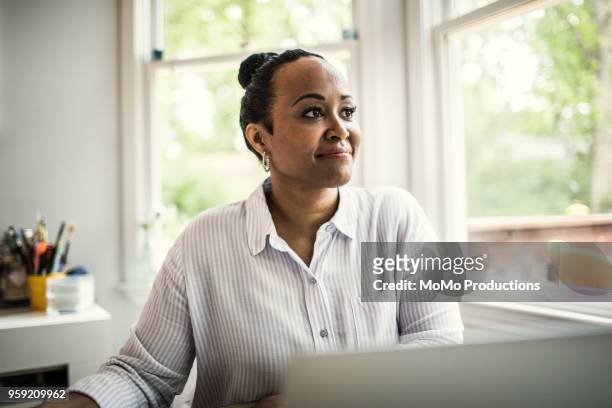 woman working on laptop in kitchen - only mature women stock pictures, royalty-free photos & images