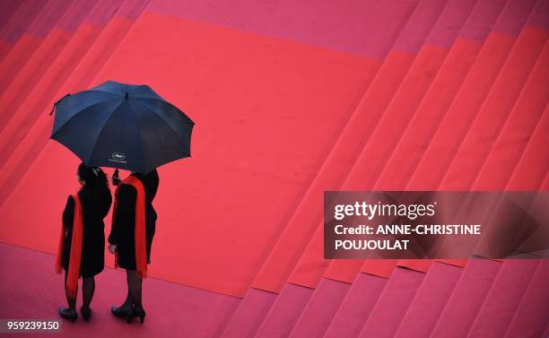 Hostesses hold an umbrella as they wait under the rain on the red carpet on May 16, 2018 before the screening of the film "Burning" at the 71st...