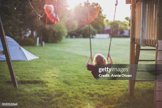 kids swinging on swing set - spielplatz einrichtung stock-fotos und bilder