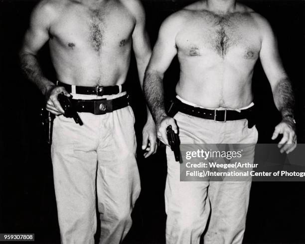 View, from the neck down, of a pair of shirtless police officers, both with their guns drawn, New York, New York, July 20, 1941. The officers dove...