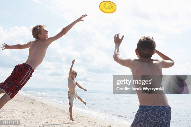 three boys playing frisbee on the beach - frisbee fotografías e imágenes de stock