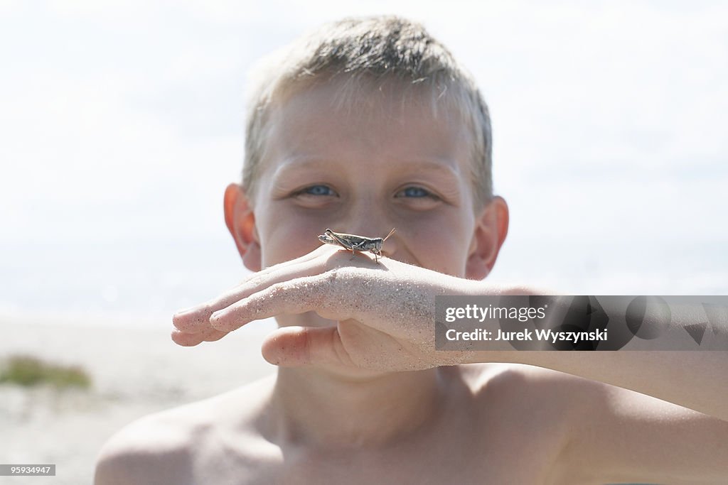 Smiling boy holding grasshopper on his hand