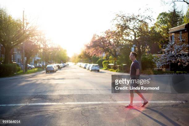 a man crossing a street at sunset - montreal street stock pictures, royalty-free photos & images