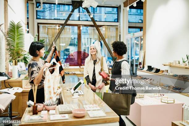 smiling friends in discussion with shop owner while checking out after shopping in boutique - older women in short skirts stock pictures, royalty-free photos & images