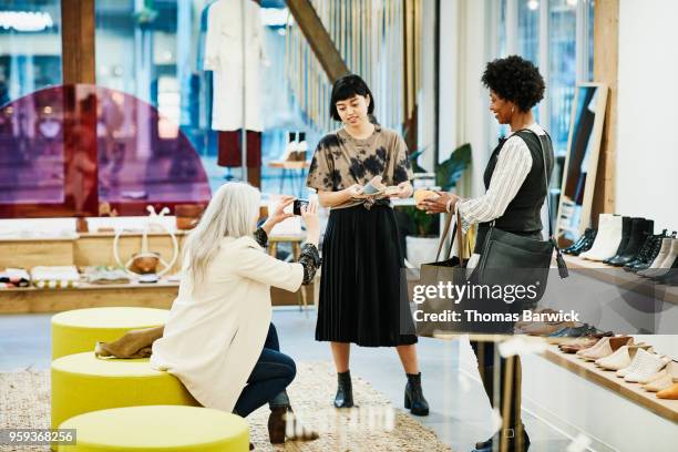 woman taking photo of shoes with smartphone while shopping with friend in boutique - older women in short skirts stock pictures, royalty-free photos & images