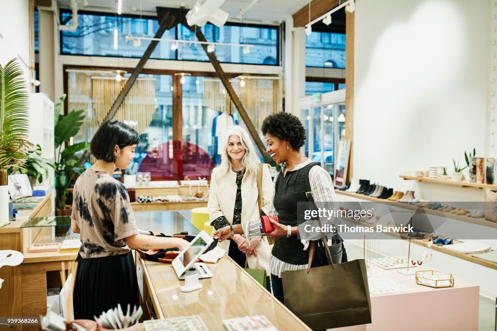 Laughing woman looking at shirt while checking out after shopping in boutique with friend