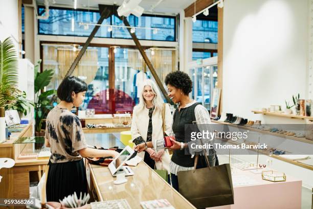 laughing woman looking at shirt while checking out after shopping in boutique with friend - older women in short skirts stock pictures, royalty-free photos & images