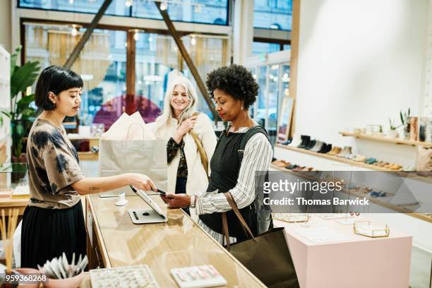 Woman paying with smartphone after shopping in boutique with friend