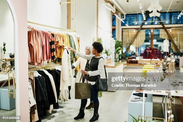 mature female friends looking at coat while shopping together in clothing boutique - clothes shop fotografías e imágenes de stock