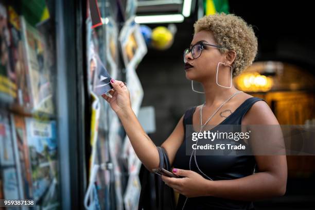 jonge vrouw op zoek naar het nieuws op de kiosk - krantenkiosk stockfoto's en -beelden