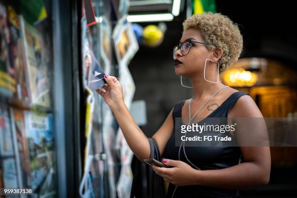 young woman looking for the news at newsstand - news stand stock pictures, royalty-free photos & images