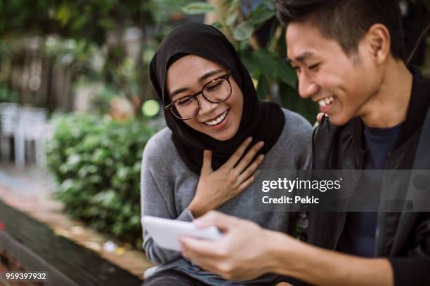 charmed by things he's shown her on phone - chinese indonesians stock pictures, royalty-free photos & images