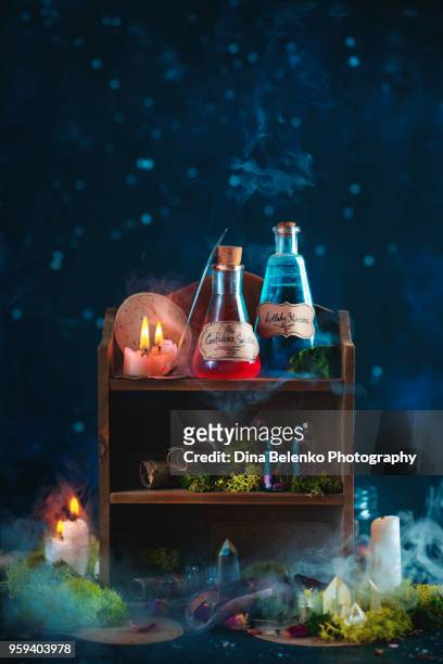 potions on a wooden shelf on witch or alchemist workplace with mysterious smoke, crystals, spell scrolls and burning candles on a dark background with copy space - setzkasten stock-fotos und bilder