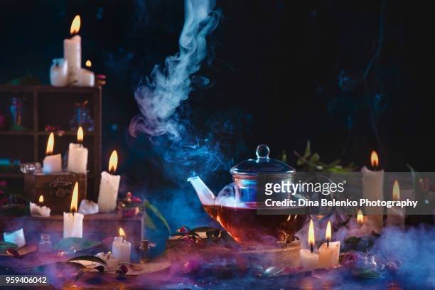 glass teapot with rising steam in a dark still life with burning candles and smoke. making herbal tea concept with copy space. - bruja fotografías e imágenes de stock