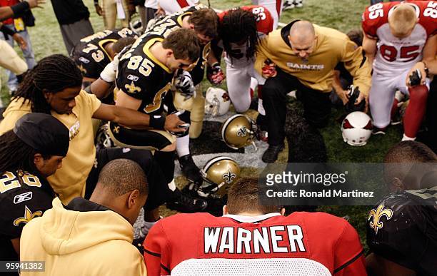 Kurt Warner of the Arizona Cardinals kneels and prays with players from both the Cardinals and the New Orleans Saints after the Saints won 45-14...