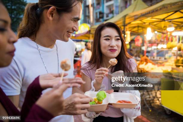 genieten van street food naar een lokale avondmarkt - straatvoedsel stockfoto's en -beelden