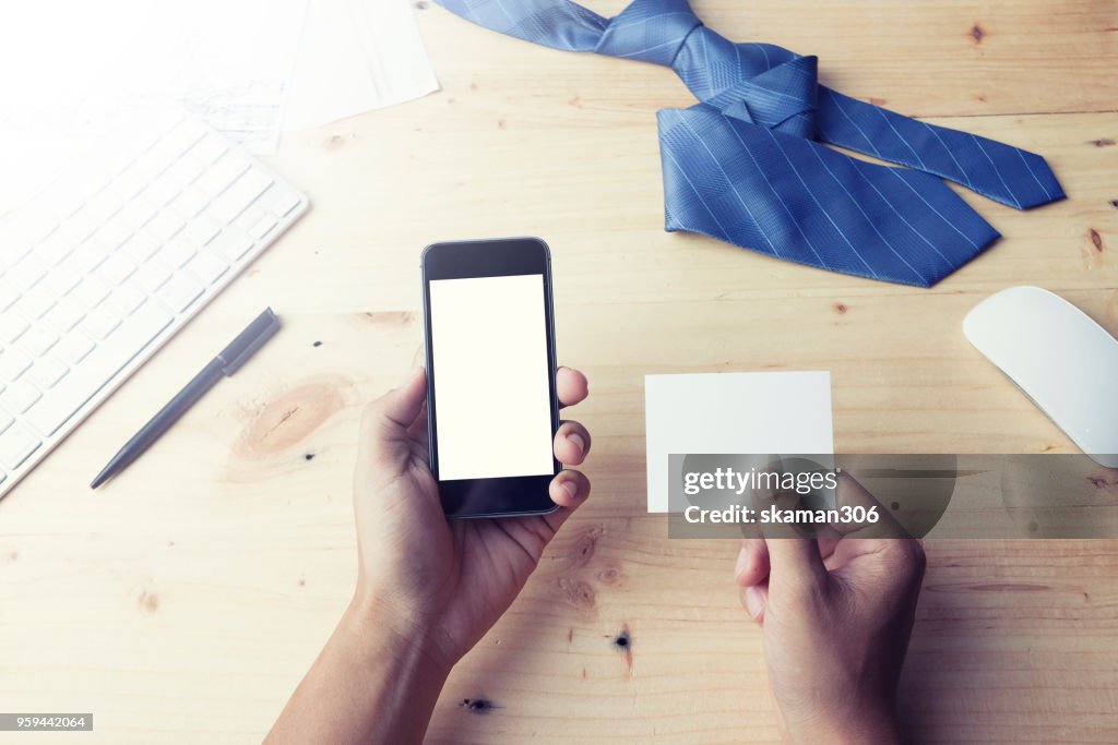 Man's hands holding a blank card and using smart phone for business