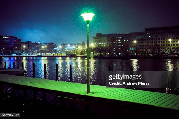 bright green illuminated street light on snow covered wooden jetty with bay, harbor and city lights reflected on the water, helsinki, finland - bright 2017 film stock pictures, royalty-free photos & images