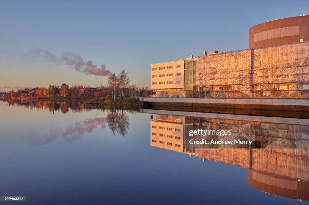 Sunset on the Oulujoki River with blue sky, new buildings, smokestacks and smoke clouds reflected in the water, Oulu, Finland