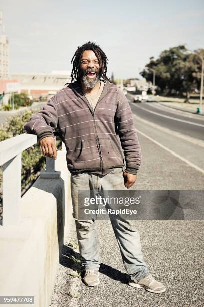 cheerful homeless man stands on a bridge - homeless man stock pictures, royalty-free photos & images
