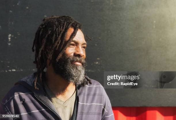 sem-teto homem com dreadlocks e barba sorrisos melancolicamente - homeless person - fotografias e filmes do acervo