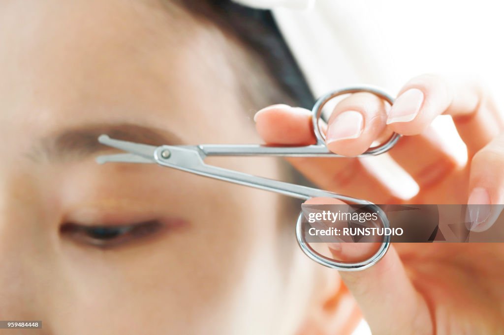 Close-up of a young woman tweezing eyebrows