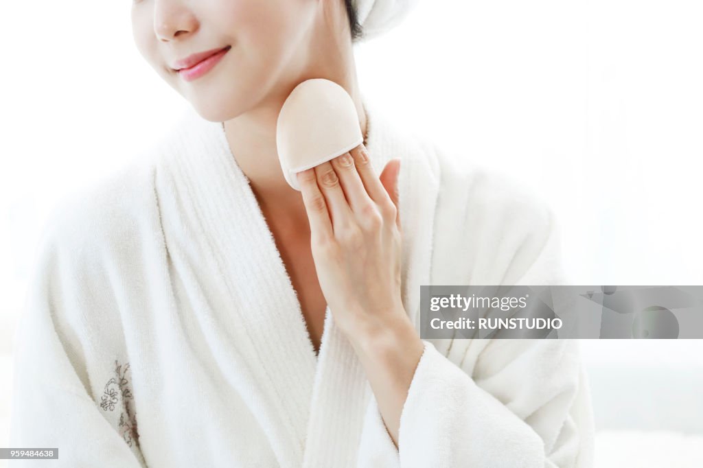 Young woman applying body powder on neck