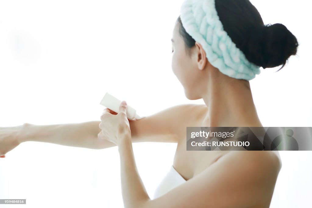 Young woman applying body lotion on arm