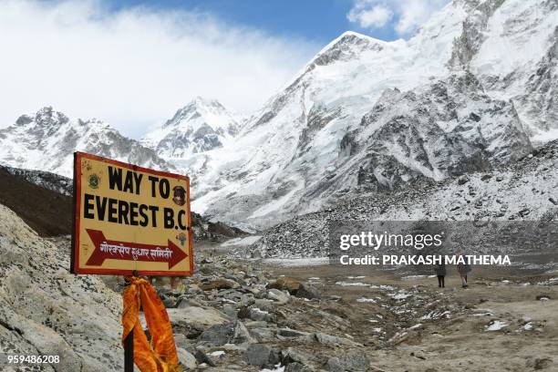 In this photograph taken on April 26 a sign points towards the Everest base camp while two trekkers walk in the Everest region in Solukhumbu district...