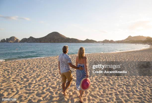 pareja caminando hacia los cerros en la playa por el mar al atardecer - cabo san lucas fotografías e imágenes de stock