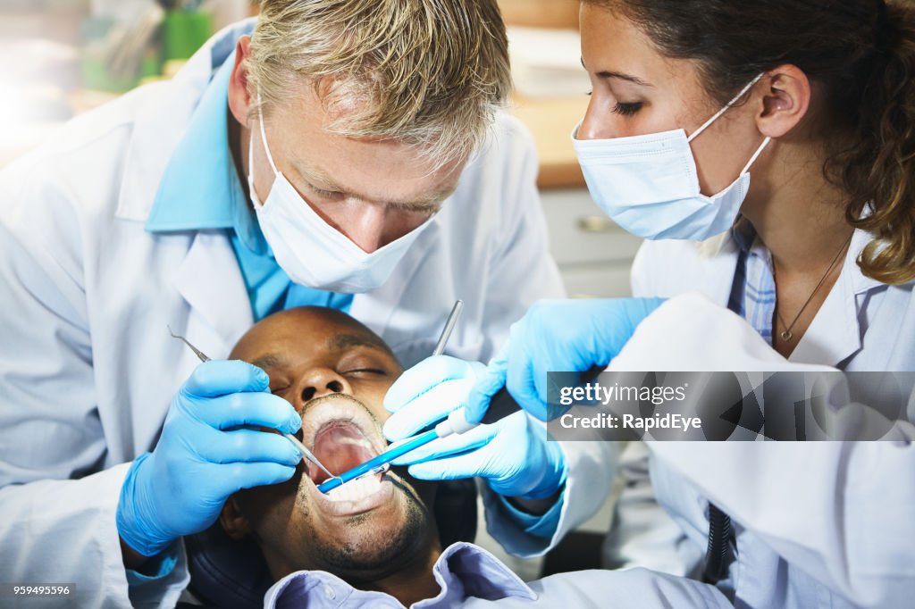 Dentist working on patient's teeth, assistant standing by