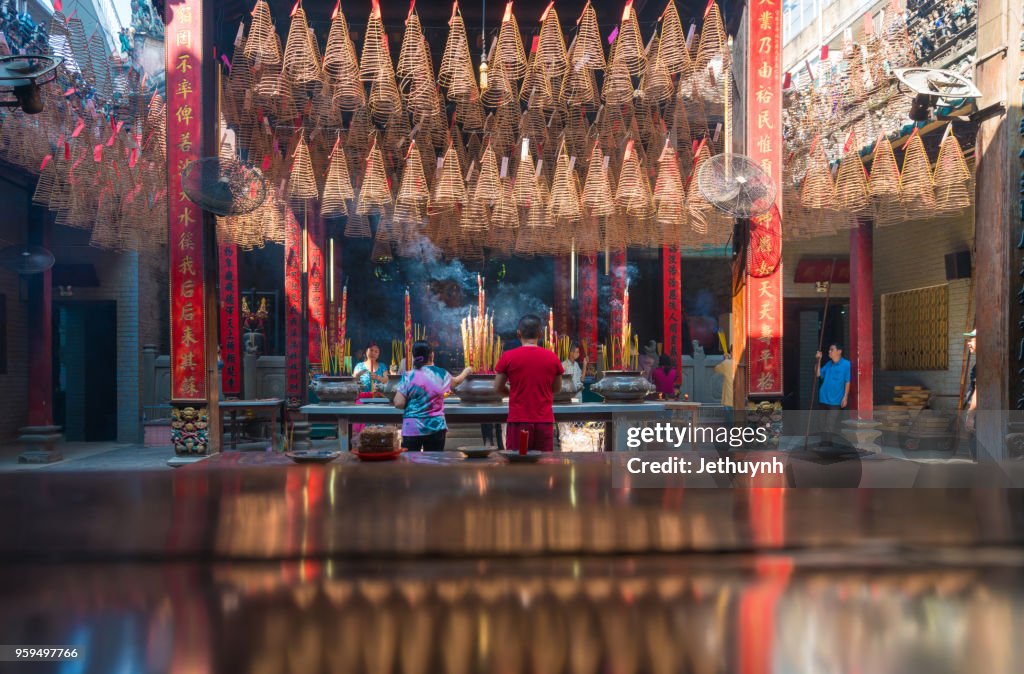 People praying Inside Thien Hau Pagoda Cholon, Ho Chi Minh City. Pagoda for the Cantonese Congregation. Incense burning on the central table with incense prayers above.