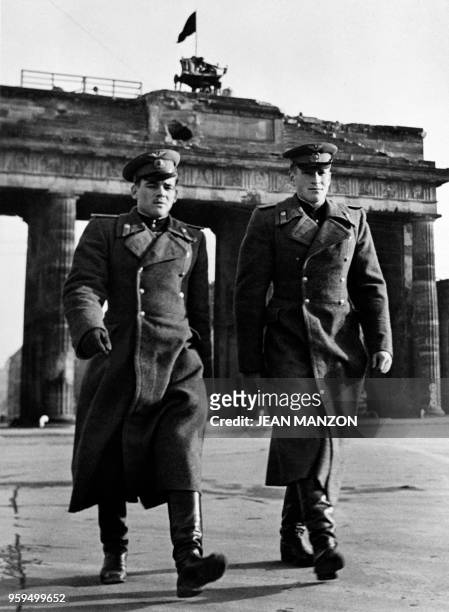 Two soviet soldiers walk together as the red flag floats on the Brandenburg gate, located on the demarcation line between russian and british zones...
